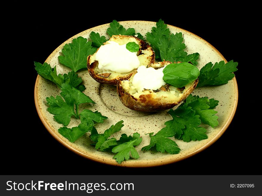 Halved baked potato on a plate surrounded by parsley's leaves on a black. Halved baked potato on a plate surrounded by parsley's leaves on a black