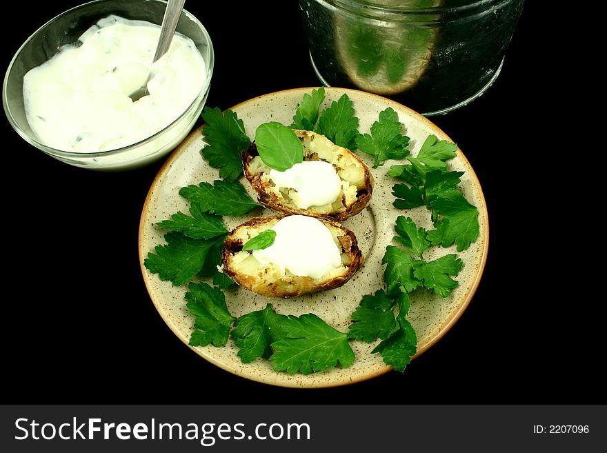 Halved baked potato on a plate surrounded by parsley's leaves together with souce. Halved baked potato on a plate surrounded by parsley's leaves together with souce