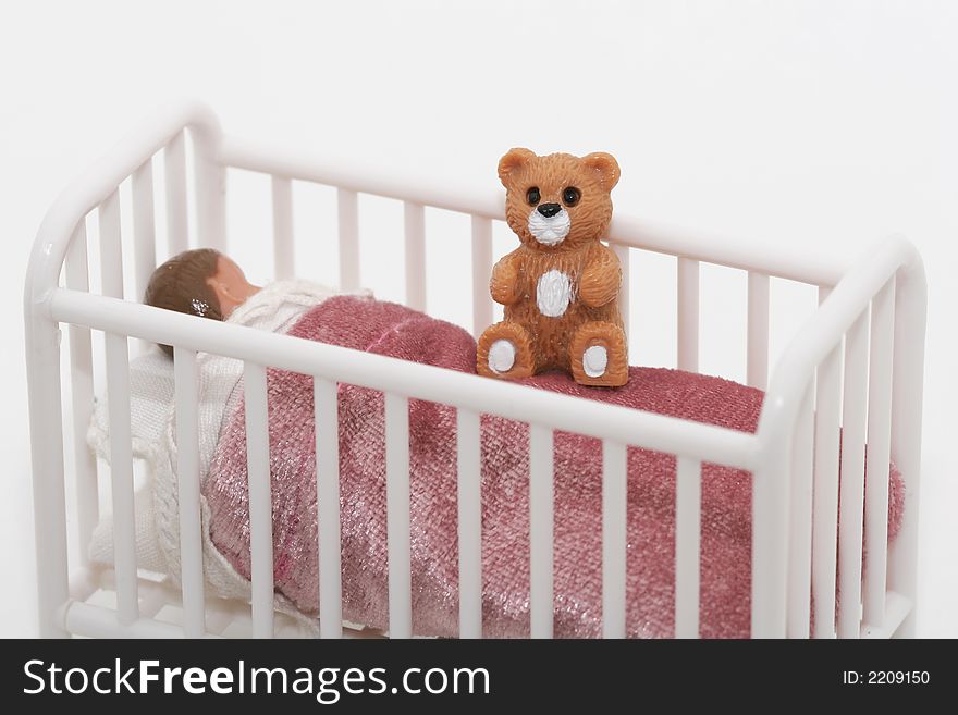 A close up of a toy sleeping child in crib bed with teddy bear, shot on white. A close up of a toy sleeping child in crib bed with teddy bear, shot on white