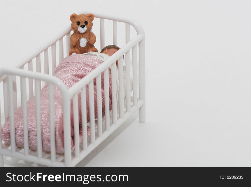 A close up of a toy sleeping child in crib bed with teddy bear, shot on white. A close up of a toy sleeping child in crib bed with teddy bear, shot on white