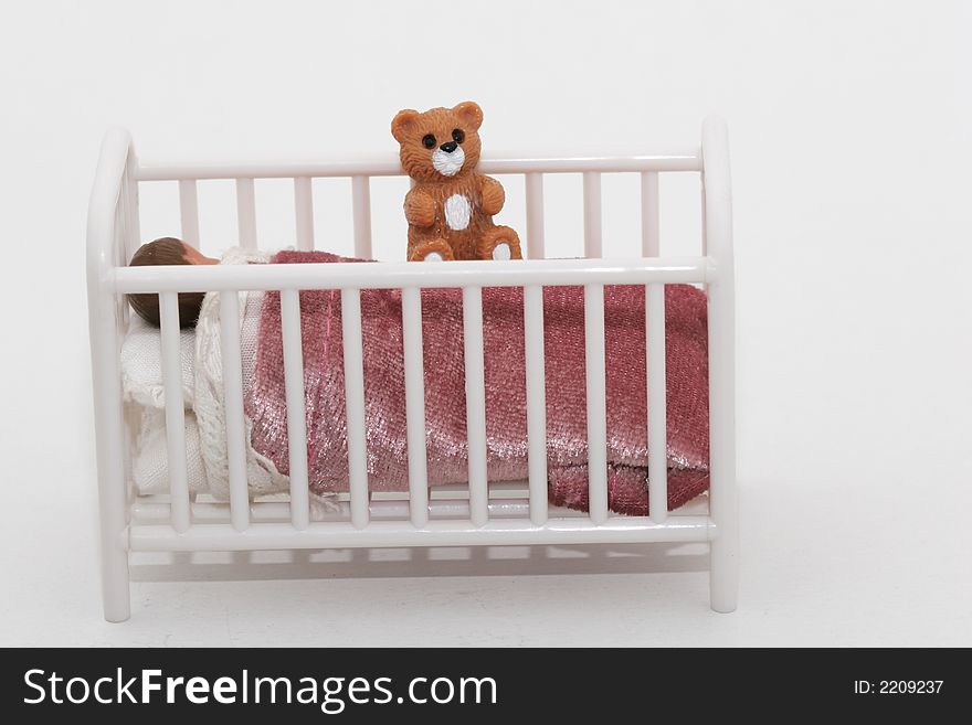 A close up of a toy sleeping child in crib bed with teddy bear, shot on white