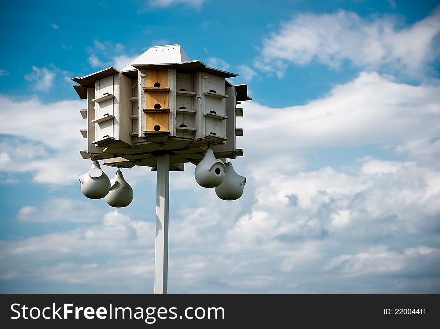 A wooden bird condo (large bird house) set against a cloudy blue sky. A wooden bird condo (large bird house) set against a cloudy blue sky.