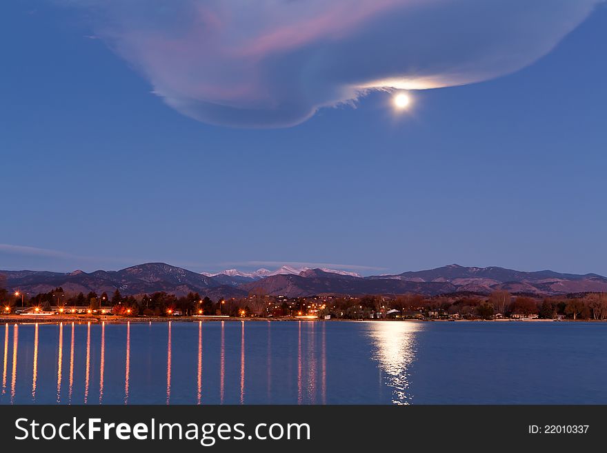 Full moon over urban lake at dawn, with snow capped mountains, light reflections and interesting cloud formation. Full moon over urban lake at dawn, with snow capped mountains, light reflections and interesting cloud formation.