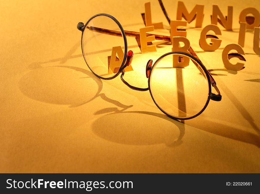 Reading concept. Old spectacles on yellow paper surface with cutting letters. Reading concept. Old spectacles on yellow paper surface with cutting letters