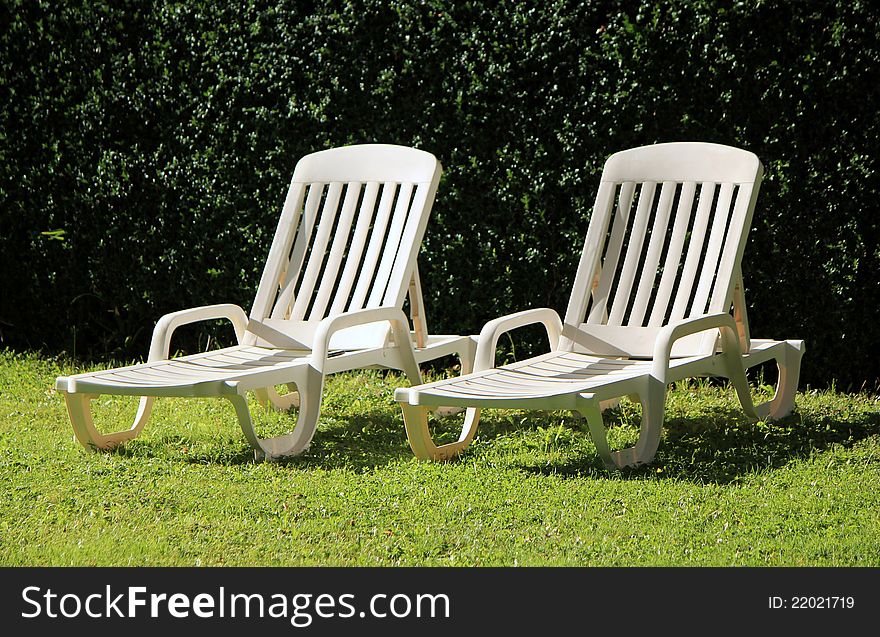 Two white lawn chairs in a green garden by summer. Two white lawn chairs in a green garden by summer