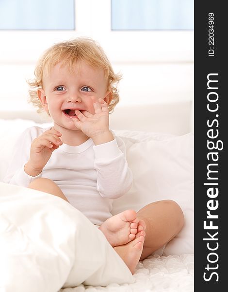 Little boy sitting on a white bed, smiling. Little boy sitting on a white bed, smiling