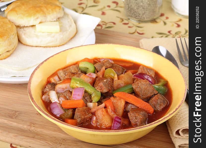 Bowl of beef stew with buttered biscuit in background. Bowl of beef stew with buttered biscuit in background