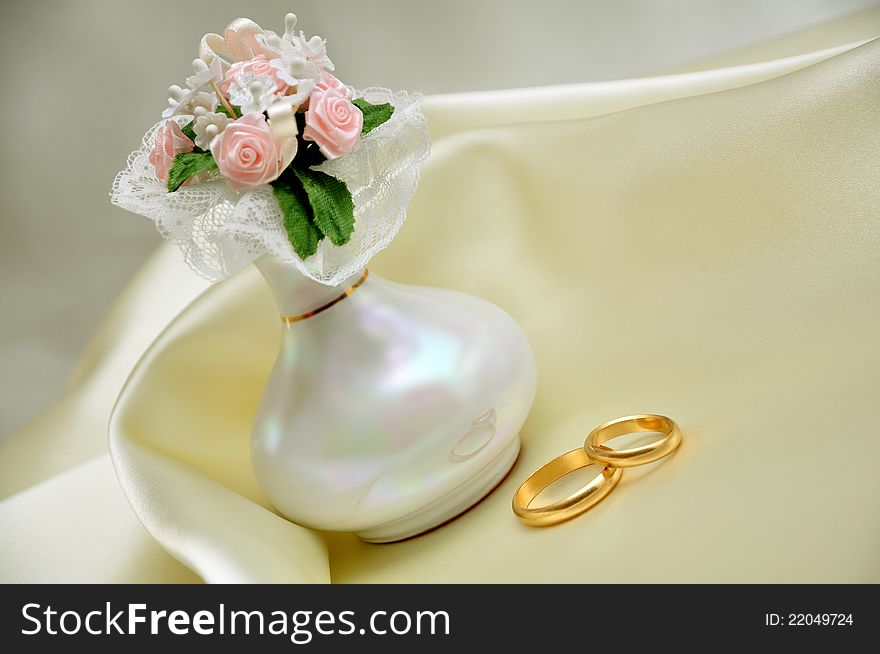 Wedding rings over ivory silk with roses bouquet in vase. Wedding rings over ivory silk with roses bouquet in vase