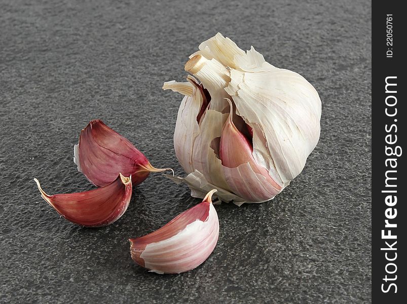 A garlic bulb and three individual cloves on a dark textured background. A garlic bulb and three individual cloves on a dark textured background.