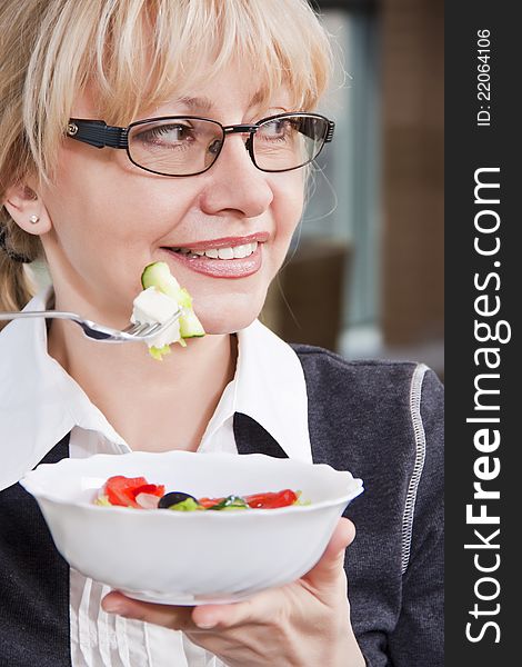 Adult blonde woman in glasses eats salad in a bright room