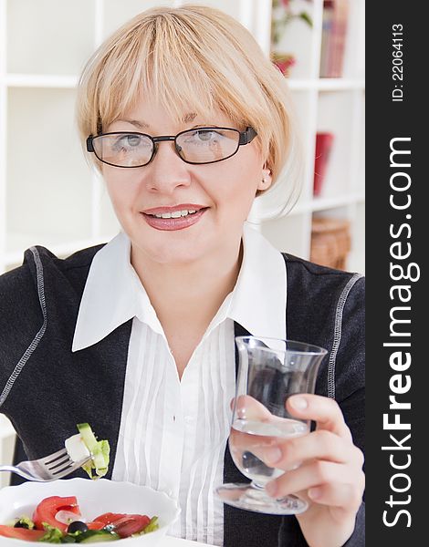 Adult blonde woman in glasses eats salad in a bright room