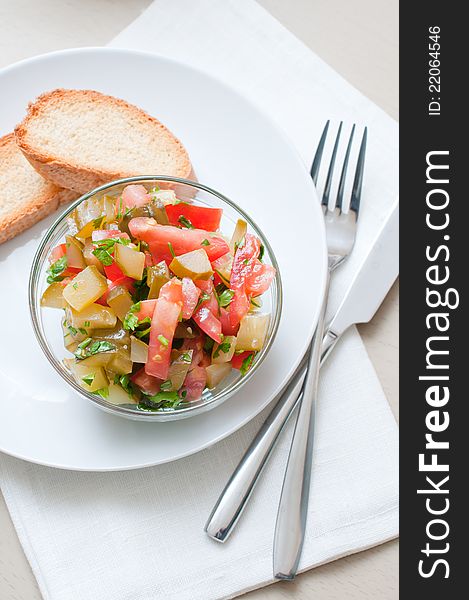 A bowl of salad made of cucumbers and tomatoes and croutons on a white plate.