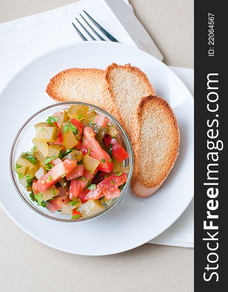 A bowl of salad made of cucumbers and tomatoes and croutons on a white plate.