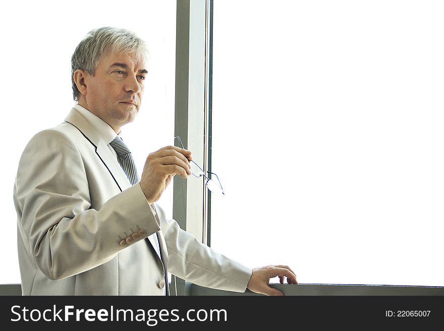 Male middle-aged businessman standing at the window and thinking. Male middle-aged businessman standing at the window and thinking