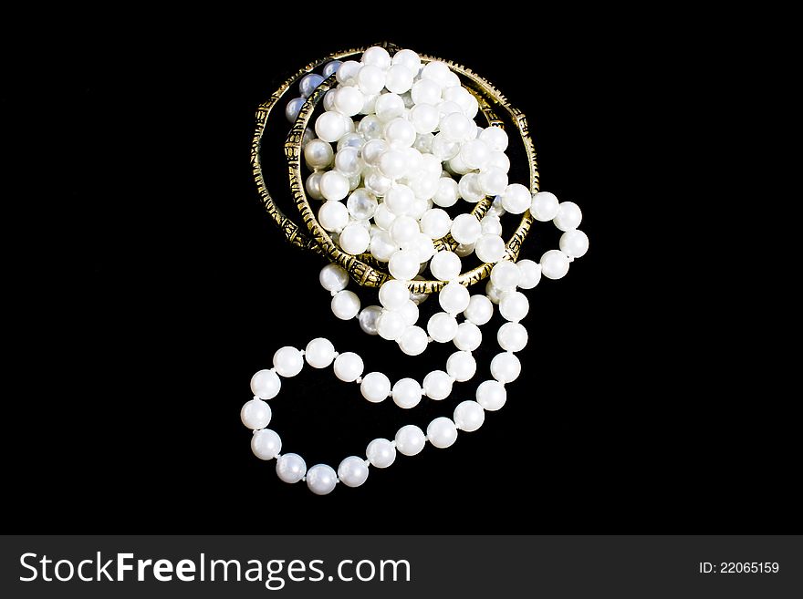 Bundled fashion pearls over a couple of brass bracelets on black background. Bundled fashion pearls over a couple of brass bracelets on black background.