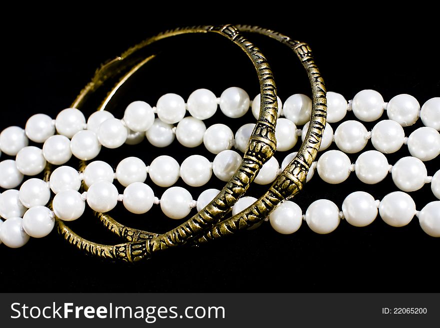 Two brass bracelets and a line of fashion pearls over black background. Two brass bracelets and a line of fashion pearls over black background.