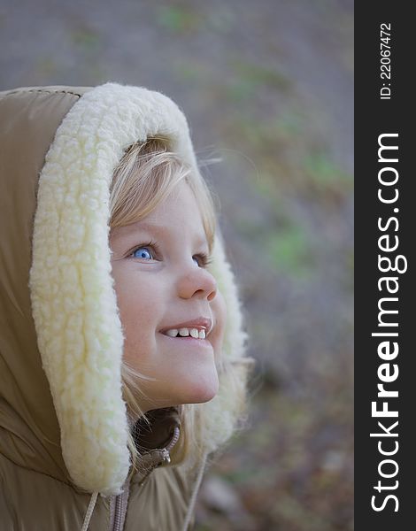 Blue-eyed girl smiling and looking up. Fall and cold, so a child wearing a hood. Blue-eyed girl smiling and looking up. Fall and cold, so a child wearing a hood