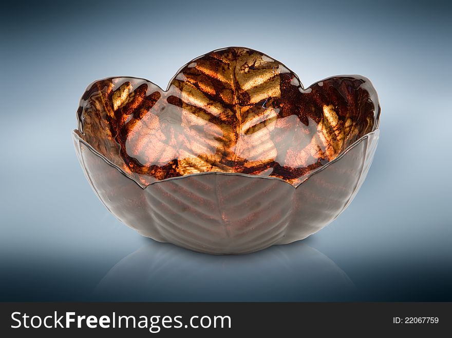 Orange glass vase with leaf like texture against blue reflective background. Orange glass vase with leaf like texture against blue reflective background