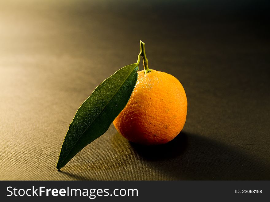 Ripe tangerine with green on a black background. Ripe tangerine with green on a black background