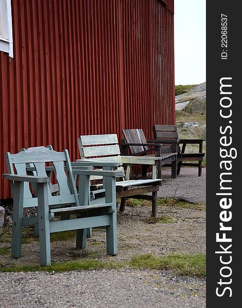 four pair of chairs outside a red old house close by the see in sweden. The shairs have different color
and positions.