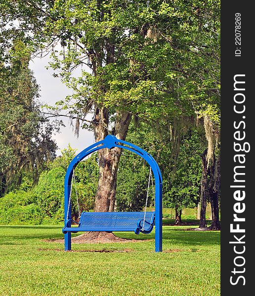 A rocking bench painted blue surrounded by grass, with trees as background. Vertical view. A rocking bench painted blue surrounded by grass, with trees as background. Vertical view