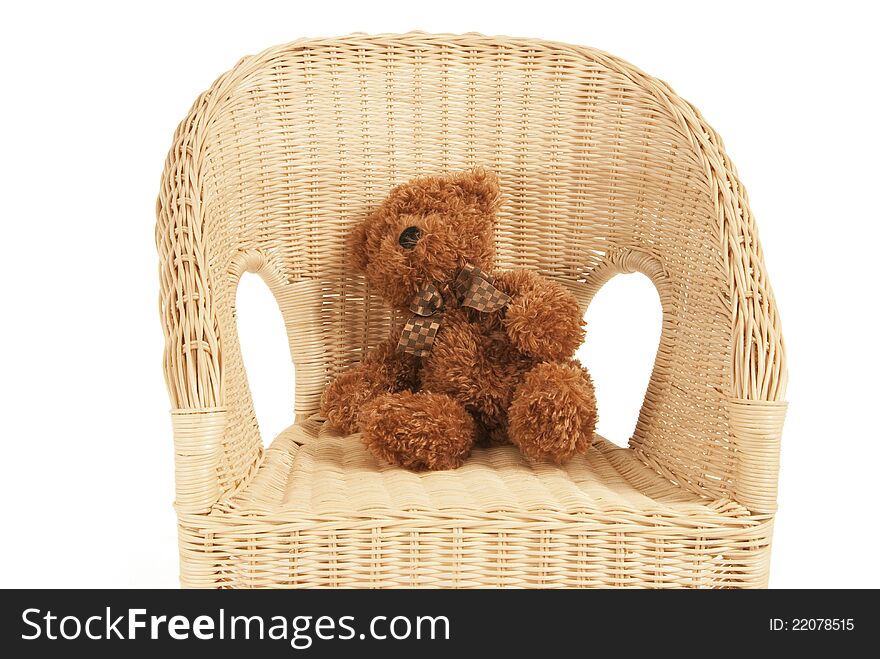 This is a brown teddy bear seating on a rattan chair isolated over a white background. This is a brown teddy bear seating on a rattan chair isolated over a white background.