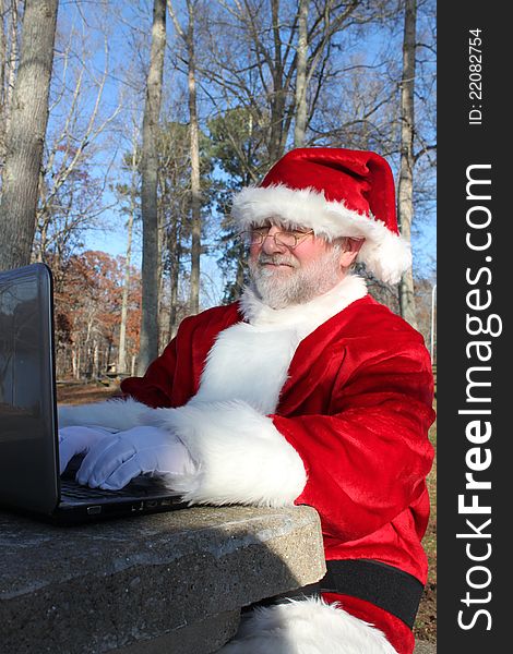 Santa sitting at a park table doing some last minute online shopping on his computer. Santa sitting at a park table doing some last minute online shopping on his computer.