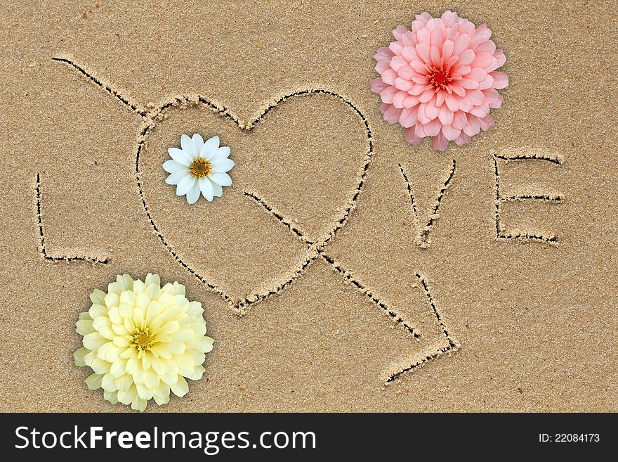 Love word with love symbol and flowers on sand. Love word with love symbol and flowers on sand