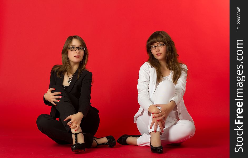 Young pretty sisters twins posing sitting in studio on red background