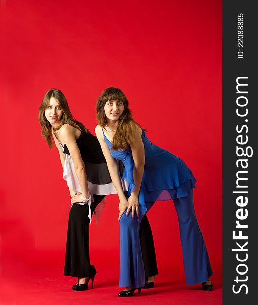 Young pretty sisters twins posing staying in studio on red background
