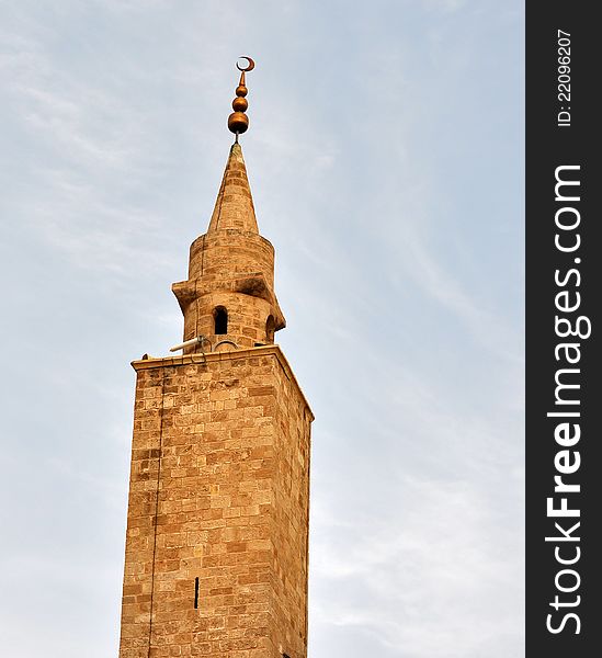A Mosque minaret made of sand stone with a bronze crescent that tops it. A Mosque minaret made of sand stone with a bronze crescent that tops it