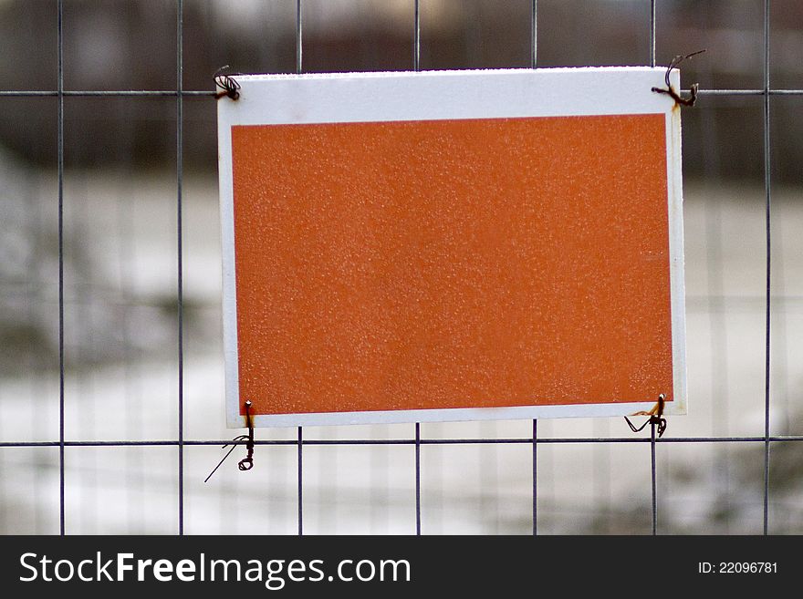 Blank orange sign attached to metal fence. Blank orange sign attached to metal fence.