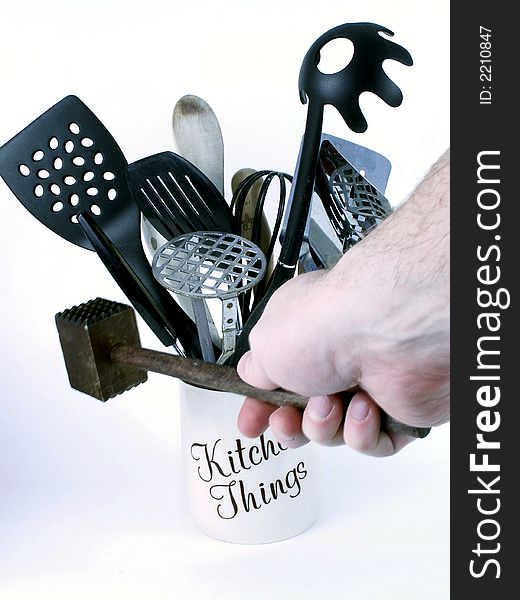 Man's hand grasps wooden meat tenderizer, with kitchen utensils in background. Man's hand grasps wooden meat tenderizer, with kitchen utensils in background.