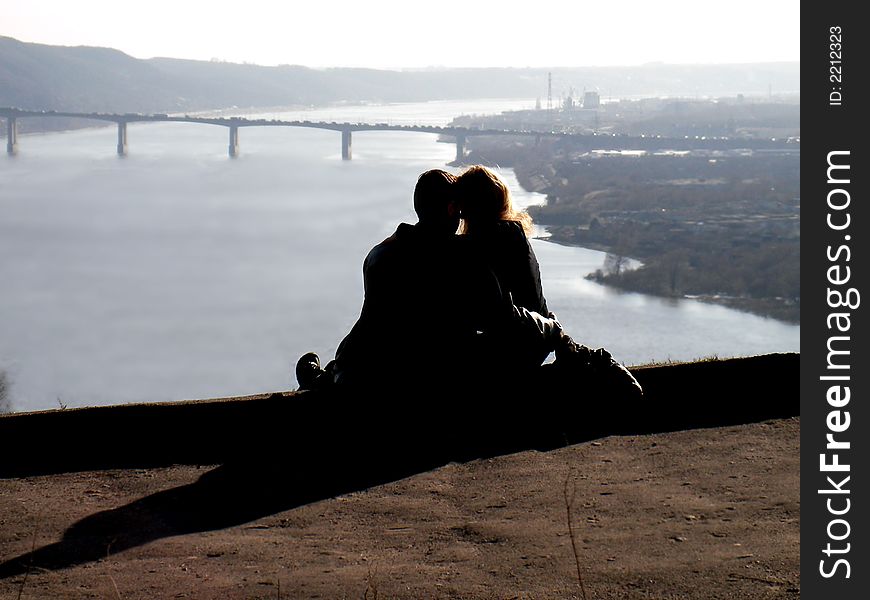 Amorous pair at a rock above a river. A time stoped. Even cars put up on the bridge
