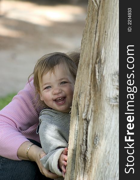 A 19 months old Israeli girl, smiling behind a tree.