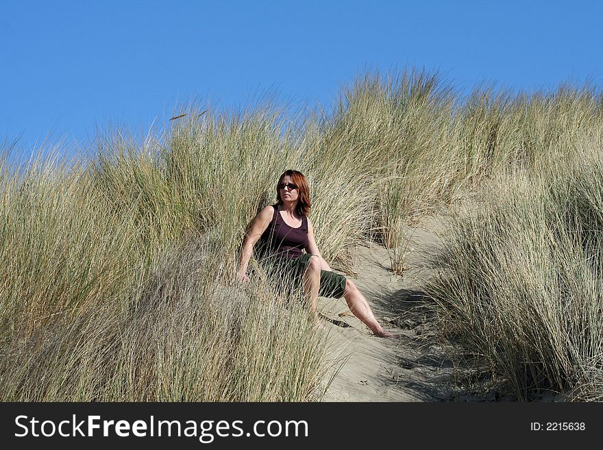 Lady sitting high up in the grassy area off the sandy beach. Lady sitting high up in the grassy area off the sandy beach