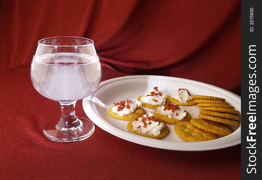 Wine glass with cracker snacks against a red drapped background.