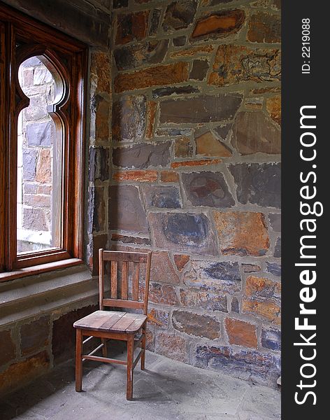 A single wooden chair by the window on a stone porch. A single wooden chair by the window on a stone porch