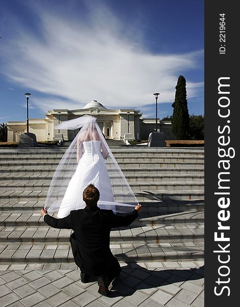 Groom holding brides veil while kneeling from behind. Groom holding brides veil while kneeling from behind