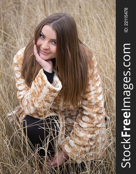 Nice girl in a fur coat sitting on a background of wheat field