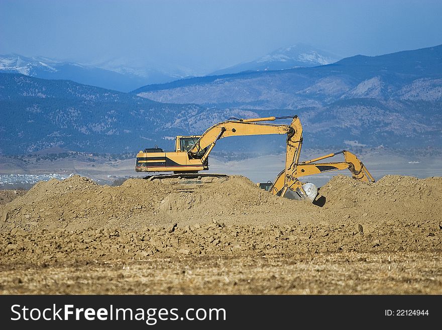 A pair of excavators moves dirt at a construction site. A pair of excavators moves dirt at a construction site.