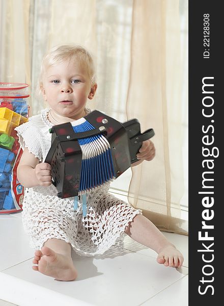 The little girl in a white dress sits on a window sill and plays an accordion