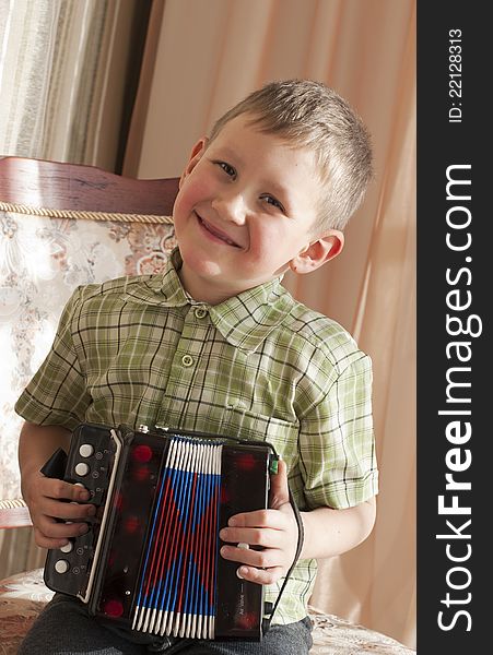 The little boy  sits on chair and plays an accordion