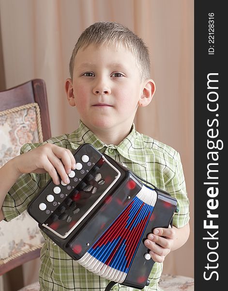 The little boy sits on chair and plays an accordion