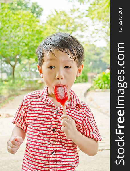 Young asian boy eating fruit flavour ice-cream in park. Young asian boy eating fruit flavour ice-cream in park