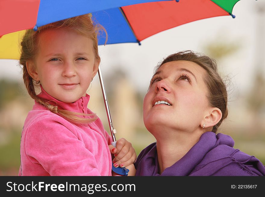 Girl and mom are hiding under the umbrella of color fall. Girl and mom are hiding under the umbrella of color fall
