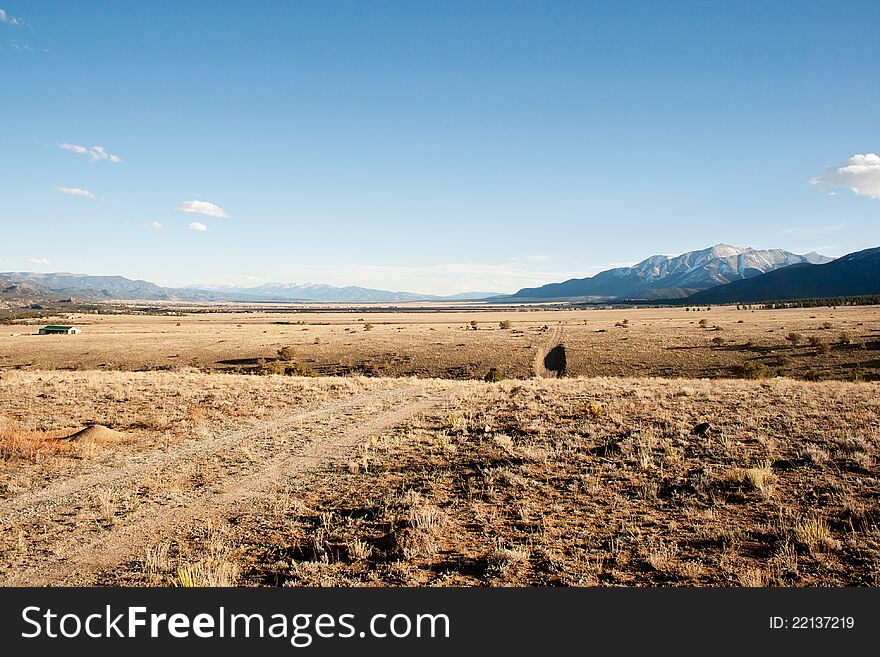 A dry pasture with a dirt road running through it. Mountains lie in the background. A dry pasture with a dirt road running through it. Mountains lie in the background