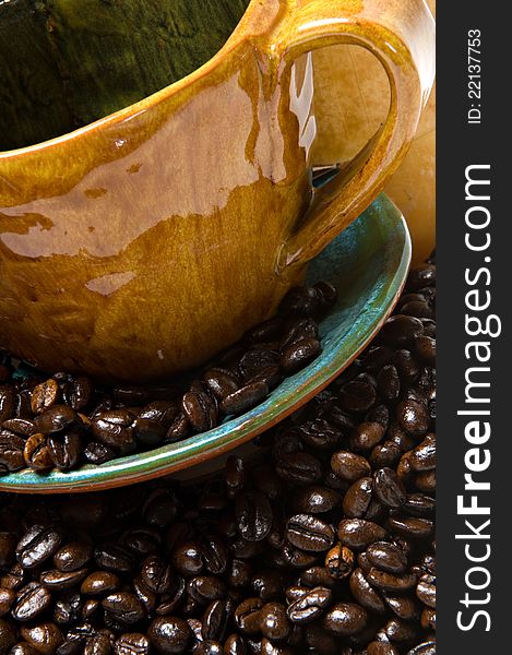 Close up of a coffee mug and saucer overflowing with dark roasted coffee beans.  Shallow depth of field. Close up of a coffee mug and saucer overflowing with dark roasted coffee beans.  Shallow depth of field.