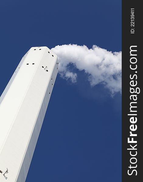 Smokestack with white smoke over blue sky