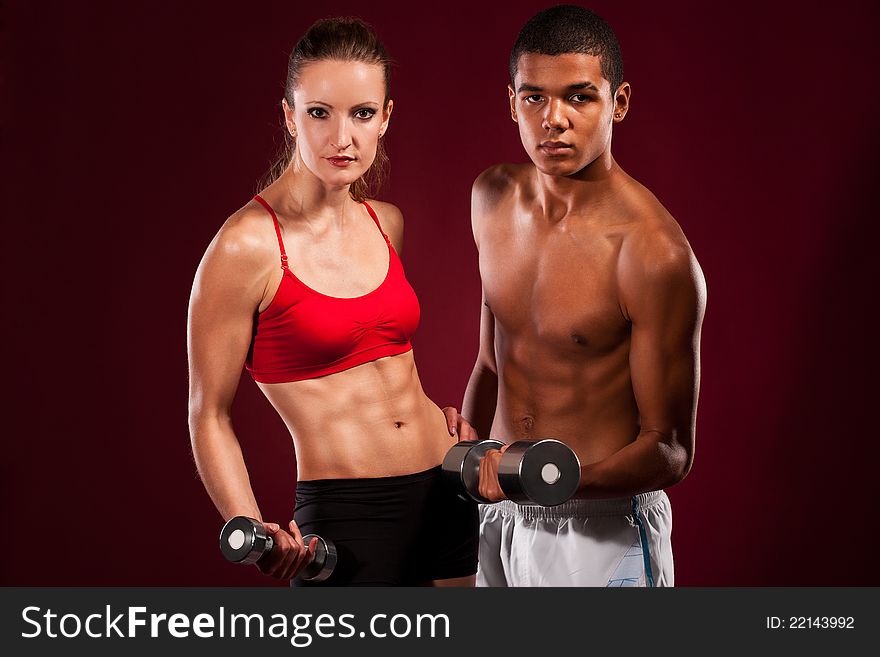 Strong young couple working out with dumbbells. Shot in studio on a red background.